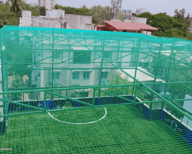 Evening view of a cricket net setup with city lights twinkling in the background.