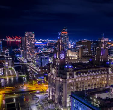 Night aerial view of Liverpool city skyline featuring the Royal Liver Building and illuminated waterfront docks.