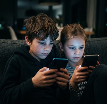 Niños usando teléfonos móviles en casa durante la noche mientras miran la pantalla de sus smartphone