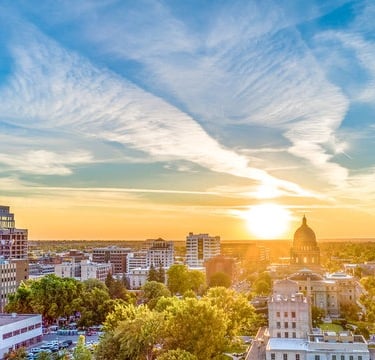 A golden sunset over the Boise, Idaho skyline featuring the State Capitol building and downtown city buildings.