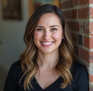 Smiling woman with wavy brunette hair posing for a professional headshot against a brick wall.