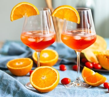 two glasses of aperol spritz with oranges and cranberries