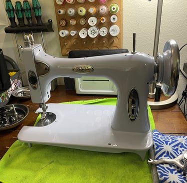 Vintage White sewing machine on a wooden workbench with thread spools and tools.