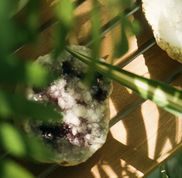 Weiße Kristallgeode mit violetten Akzenten auf Holz, umgeben von grünen Blättern.