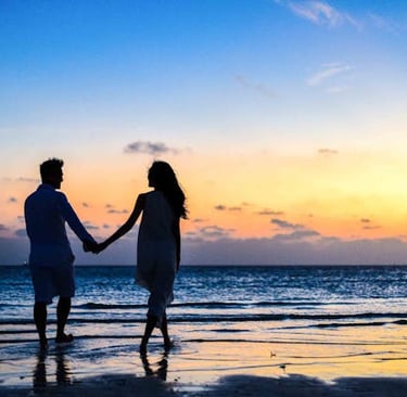 A romantic couple silhouette holding hands on a tropical beach during a colorful sunset.