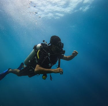 A scuba diver in full gear explores the deep blue ocean water with sunlight filtering from above.