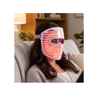 Woman relaxing on a couch while wearing a glowing red light therapy face mask.