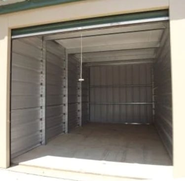 An open, 10X20 foot empty self-storage unit with clean metal walls and a roll-up door.
