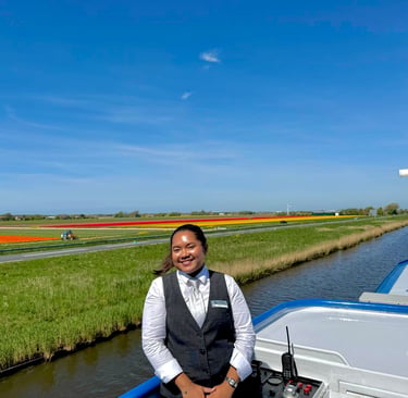 Smiling beautiful crew in staff uniform on a cruise ship passing colorful Dutch tulip fields.