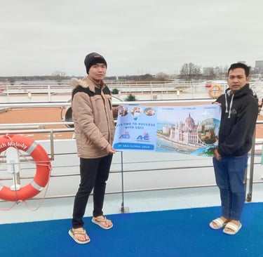 Two crewmembers hold an AKA Global Grup banner on the deck of the Dutch Melody river cruise ship.