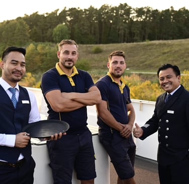A smiling professional river cruise crew in uniform posing on a ship deck with a scenic green background.