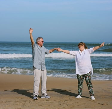 A happy senior couple holding hands and dancing on a sandy beach by the ocean waves