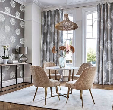 Modern dining room with gray dandelion wallpaper, round marble table, and beige velvet chairs.