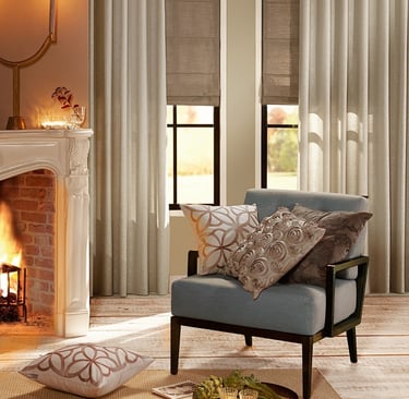 Elegant living room featuring linen drapes, roman shades, and a blue armchair by a fireplace.