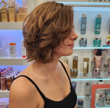 Side profile of a woman with a layered, wavy light brown bob haircut in a professional hair salon.