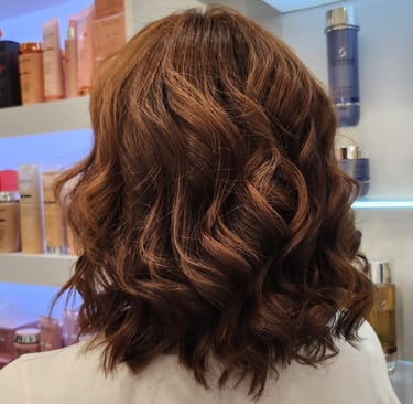 Back view of a woman with shoulder-length wavy auburn hair in a salon setting.