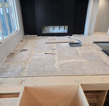 A modern living room under construction featuring a black fireplace wall and subfloor ready for hardwood flooring.