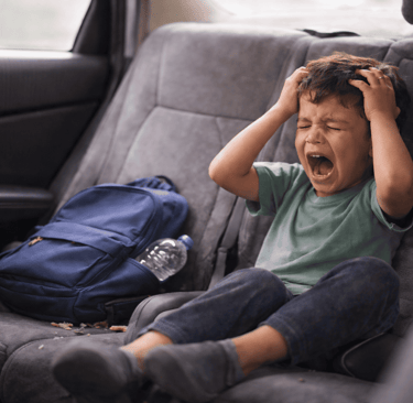 a distressed child in the  back seat with his back pack next to him