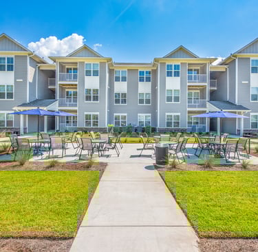Ground-level view of outdoor patio seating with umbrellas between apartment buildings at Arrogate Village in Summerville, SC