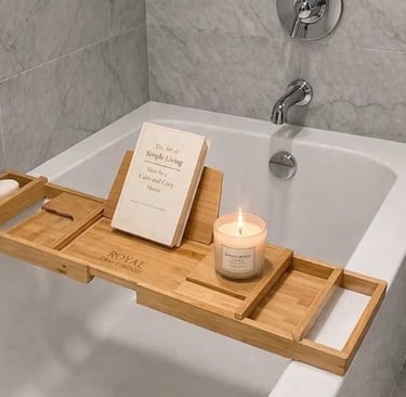 A bamboo bathtub tray caddy holds a book and a candle across a modern white soaking tub.