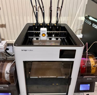 White Snapmaker J1 high-speed IDEX 3D printer with independent dual extruders on a workshop desk.