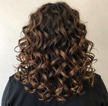 A stylist gently shaping voluminous curls with warm brown tones in an editorial-style shot