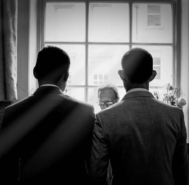 Black and white silhouette of two men in suits at a wedding ceremony standing before an officiant.