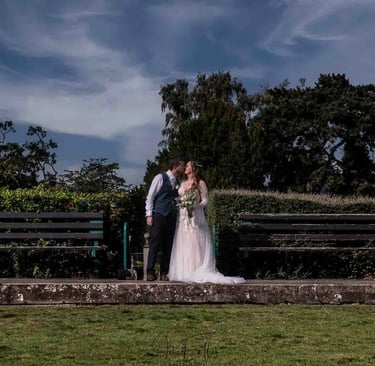 a bride and groom kissing on a bench in a park