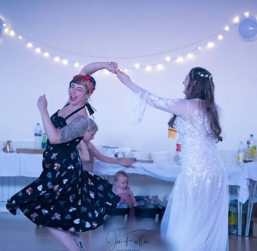 A bride and woman in a vintage dress dancing together at a wedding reception party.