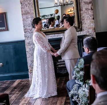 A couple exchanges vows during an indoor wedding ceremony in front of a rustic brick fireplace and mirror.