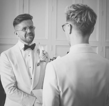 Groom in a white tuxedo exchanging vows at a black and white wedding ceremony.