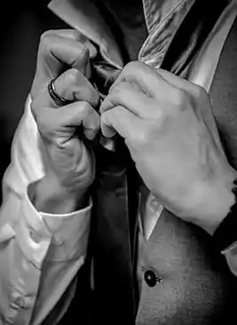 A groom in a formal waistcoat and dress shirt adjusts his necktie for a wedding ceremony.