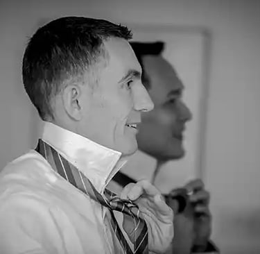 Black and white photo of two grooms tying their silk ties while getting ready for a wedding.