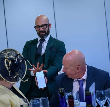 Professional magician in a green suit performing a digital phone trick for guests at a formal wedding reception.