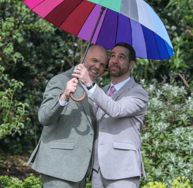 LGBTQ+ wedding couple under their rainbow umbrella