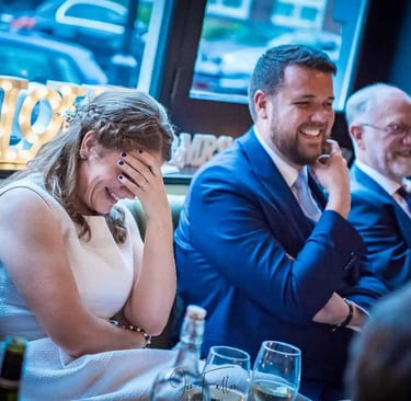 Smiling bride laughing during wedding speeches at her reception dinner.