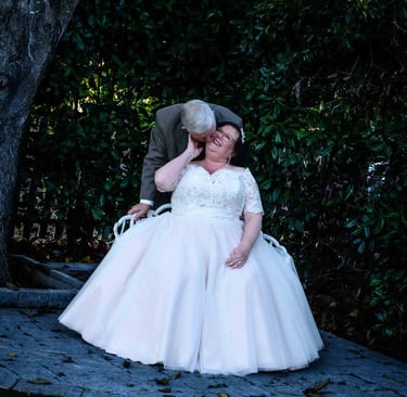 A groom kisses his smiling bride in a white lace wedding dress during an outdoor garden ceremony.