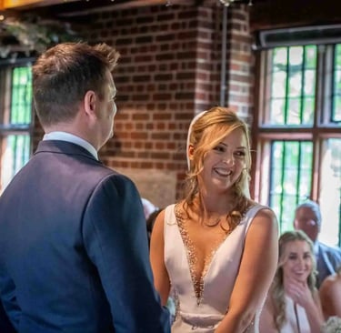 Smiling bride in a white wedding dress exchanging vows with her groom during an indoor ceremony.