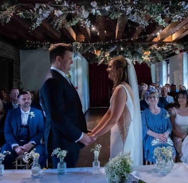 A bride and groom exchange vows in a rustic barn wedding ceremony venue with floral decor.