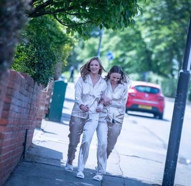 Two happy women walking on a city sidewalk wearing matching silk pajamas and slippers.