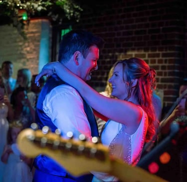 A smiling bride and groom enjoy their first dance at a rustic indoor wedding reception.