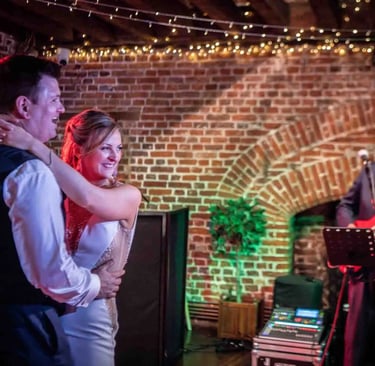 A happy bride and groom enjoy their first dance with a live wedding band in a rustic brick venue.