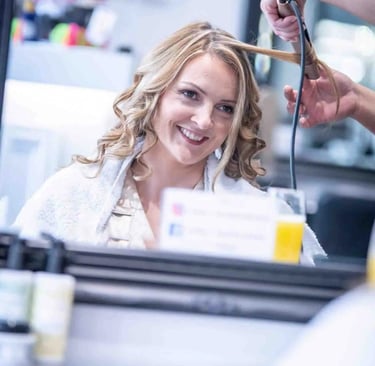 Smiling woman getting her blonde hair curled with a styling iron at a professional hair salon.