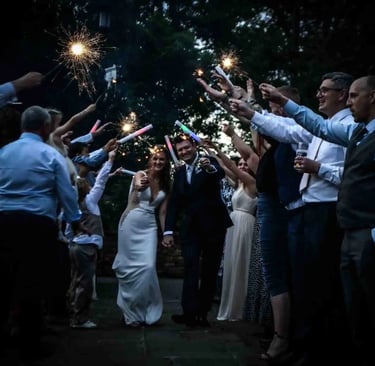 A bride and groom walk through a wedding sparkler send-off celebration at night.