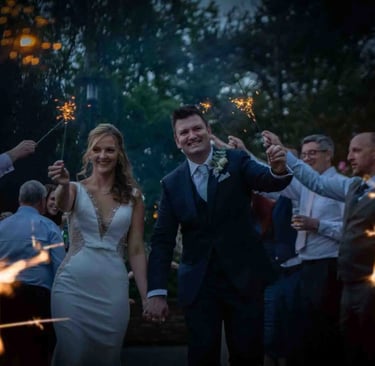 A happy bride and groom celebrate with a wedding sparkler send-off surrounded by guests outdoors at night.