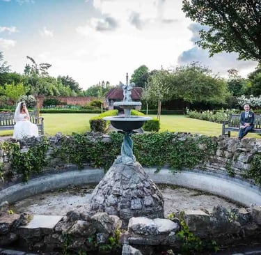 a bride and groom in a garden with a fountain
