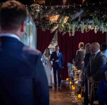 Bride and groom walking down the aisle at an indoor wedding ceremony with floral decor and candles.