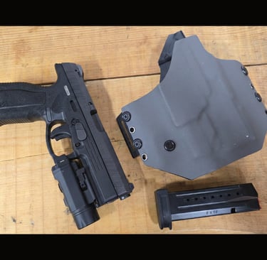 Black Steyr L9-A2 MF handgun with mounted tactical light, gray Kydex holster, and 9mm magazine on a wood surface.