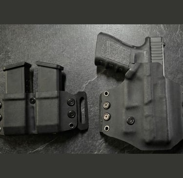 Black Kydex OWB holster with a Glock handgun and a matching double magazine carrier on a dark surface.