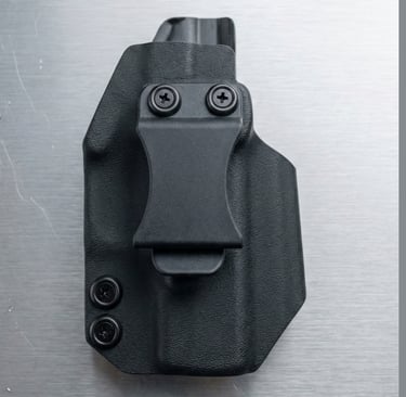 Black Kydex gun holster with a single belt clip and two retention screws, designed for concealed carry, shown on a metallic